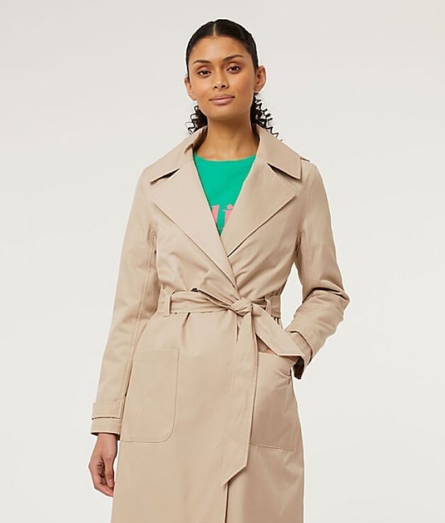 A woman wearing a beige trench coat over a green t-shirt